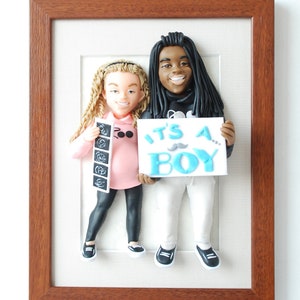 May include: A framed 3D figurine of a couple holding an ultrasound image and a sign that says "It's a Boy!" The figurine is made of clay and is painted in realistic colors. The frame is made of wood and has a brown finish.