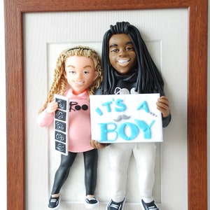 May include: A framed 3D figurine of a couple holding a sign that says "It's a Boy!" The woman is holding a sonogram picture and the man is wearing a black hoodie.