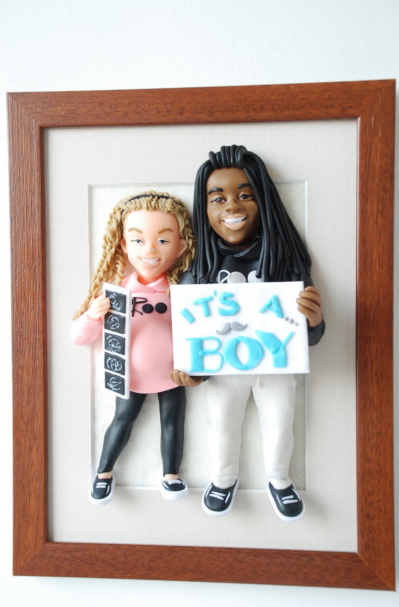 May include: A framed 3D figurine of a couple holding a sign that says "It's a Boy!" The woman is holding a sonogram picture and the man is wearing a black hoodie.