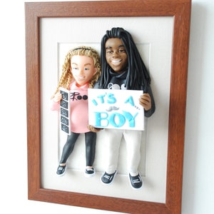 May include: A framed 3D clay sculpture of a couple holding a sign that says "It's a Boy!" The woman is holding an ultrasound picture and the man is wearing a black hoodie.