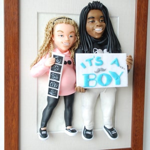 May include: A framed 3D figurine of a pregnant woman and a man holding a sign that says "It's a Boy!" The woman is holding a stack of ultrasound photos. The figurine is made of clay and painted in realistic colors.