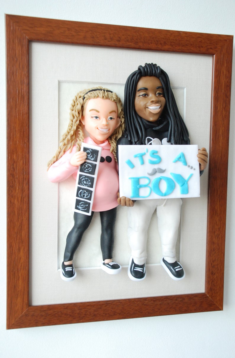 May include: A framed 3D figurine of a pregnant woman and a man holding a sign that says "It's a Boy!" The woman is holding a stack of ultrasound photos. The figurine is made of clay and painted in realistic colors.