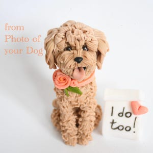 Pode incluir: Estatueta artesanal de cão castanho claro com coleira rosa e rosa. O cão está com a língua de fora e está sentado ao lado de um bloco branco com as palavras "I do too!" e um coração rosa.