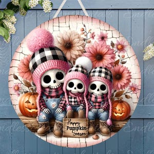 Op de afbeelding: Een rond houten bord met een roze, zwart en wit schedelontwerp. De schedels dragen roze en zwarte hoeden en sjaals. Het bord heeft een bloemige achtergrond en de tekst "Happy Pumpkin Season".