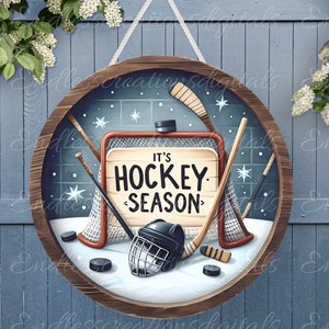 May include: A round wooden sign with a hockey theme. The sign features a hockey net, hockey sticks, a hockey puck, and a hockey helmet. The sign also has the text "It's Hockey Season" on it.