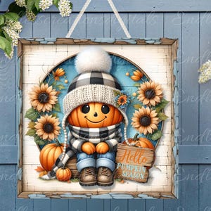 May include: A square wooden sign with a white background and a distressed wood frame. The sign features a cartoon pumpkin wearing a black and white checkered hat, a white scarf, and blue jeans. The pumpkin is sitting on a wooden ledge with sunflowers and pumpkins around it. The sign says "Hello Pumpkin Season" in a white banner.