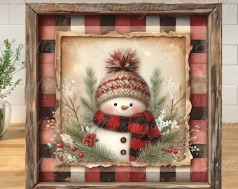 Könnte beinhalten: Eine gerahmte Illustration eines Schneemanns, der einen rot-weißen Strickhut und einen Schal trägt, umgeben von grünen Kiefernästen und roten Beeren vor einem rot-schwarzen karierten Hintergrund.