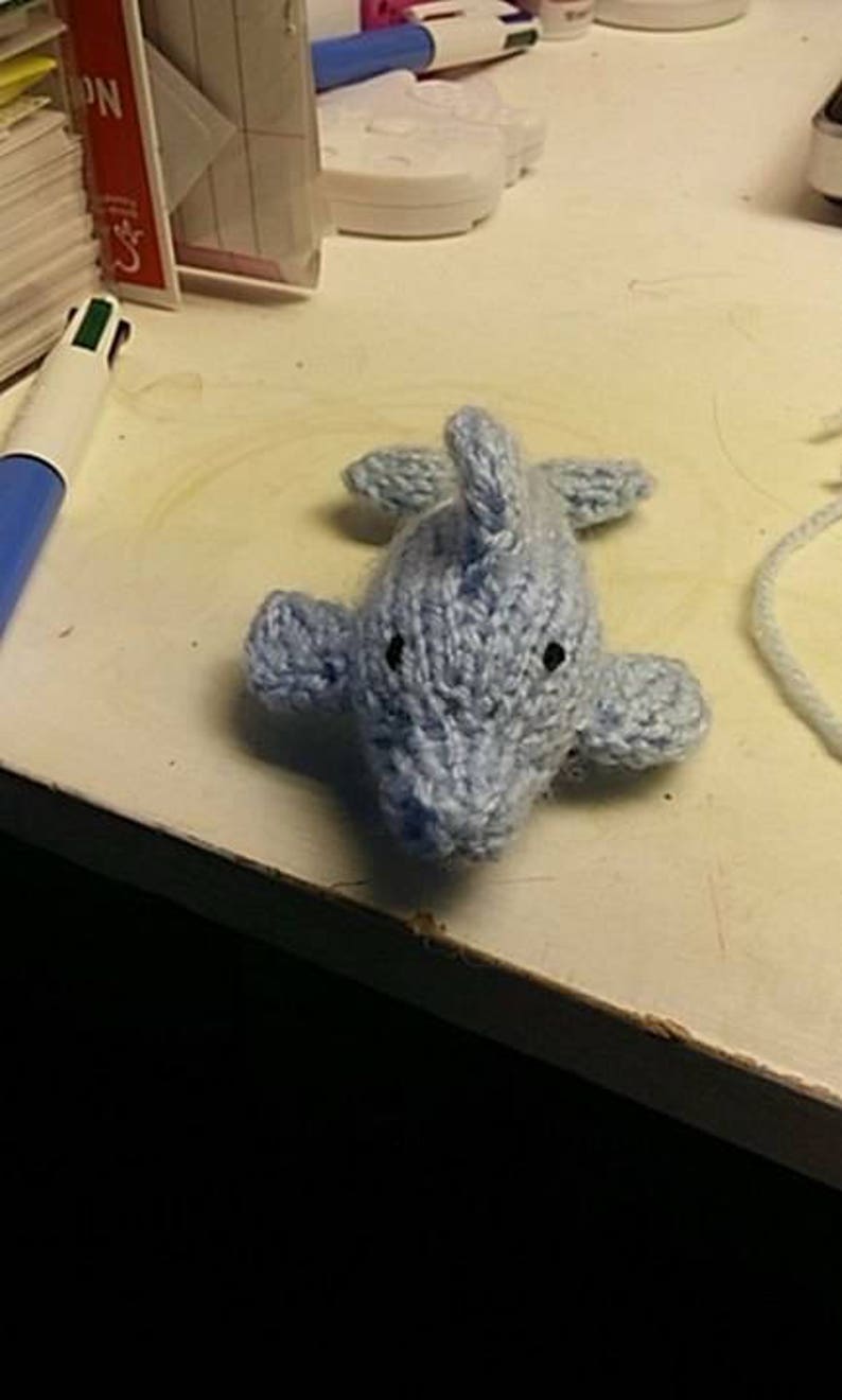 Puede incluir: Un juguete de peluche de delf&iacute;n de punto azul claro con ojos negros.