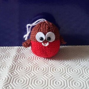 May include: A knitted red robin ornament with brown wings and white felt eyes. The robin has a white string for hanging.