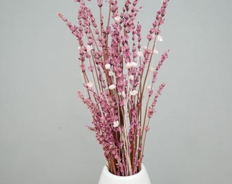 May include: A bouquet of dried pink flowers with small white accents in a white vase. The flowers have a delicate, textured appearance and are arranged in a vertical display. The vase is simple and modern, with a rounded shape.