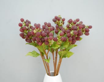 May include: A decorative artificial branch featuring clusters of dark red, textured raspberries. The branch has multiple brown stems and several bright green, serrated leaves attached to the base of the fruit clusters, creating a realistic botanical display.