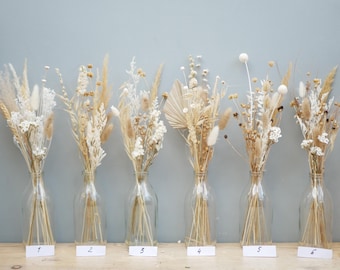 May include: Six bouquets of dried flowers in clear glass bottles, each with a unique arrangement of beige, cream, and tan grasses and blooms. The bottles are labeled with numbers 1 through 6 on white rectangular tags.