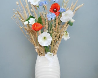 May include: A white ceramic vase with a ribbed texture holds a bouquet of dried wheat, white, blue, and orange flowers. The arrangement is set against a light blue background, creating a natural and elegant display.