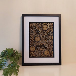 May include: Framed art print featuring a gold floral design on a black background. The artwork is displayed in a black frame with a white mat. The print showcases detailed botanical illustrations, creating a striking contrast.