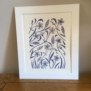 May include: A framed print of a blue and white floral design. The print features a variety of flowers and leaves, all in a stylized, graphic style. The print is set against a white background.