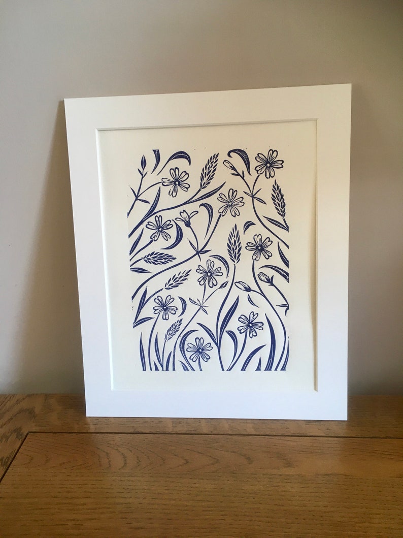 May include: A framed print of a blue and white floral design. The print features a variety of flowers and leaves, all in a stylized, graphic style. The print is set against a white background.