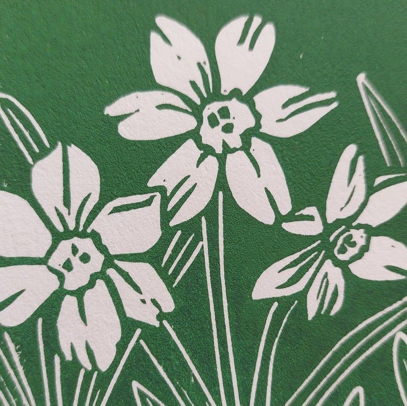 May include: A close-up of a green background with three white flowers. The flowers have five petals each and a small centre. The flowers are stylised and look like they were created using a block printing technique.