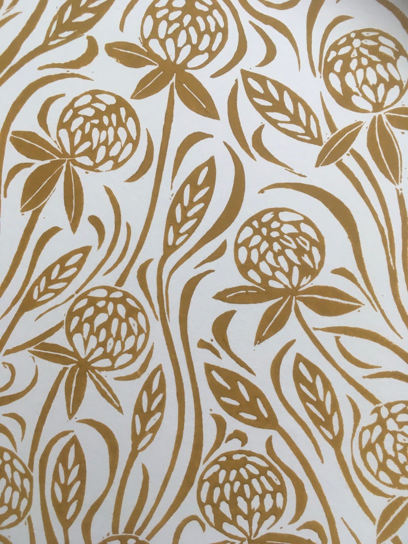 May include: A white background with a repeating pattern of gold clover flowers and leaves. The clover flowers are stylized and have a textured look.