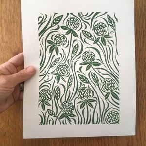 May include: A green and white print of a clover flower pattern on white paper. The print features a repeating pattern of clover flowers and leaves.