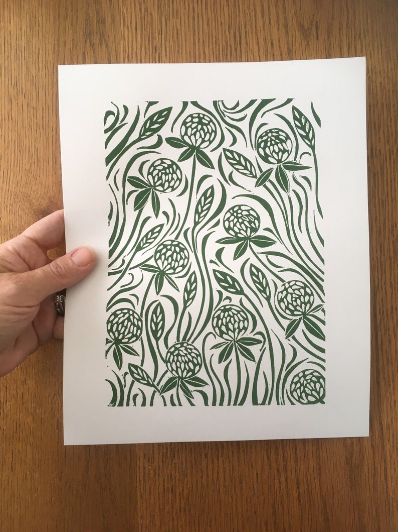 May include: A green and white print of a clover flower pattern on white paper. The print features a repeating pattern of clover flowers and leaves.