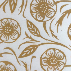 May include: A white background with a repeating pattern of gold floral designs. The flowers are stylized and have five petals. The leaves are simple and elongated. The pattern is symmetrical and balanced.