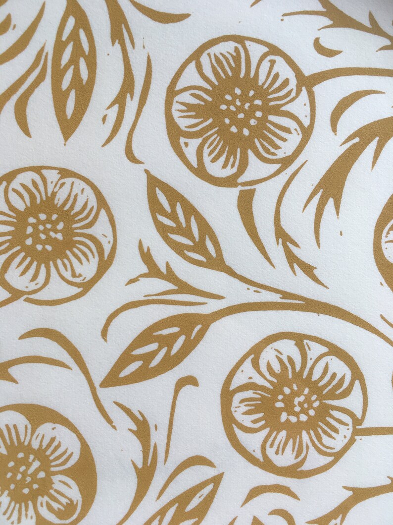 May include: A white background with a repeating pattern of gold floral designs. The flowers are stylized and have five petals. The leaves are simple and elongated. The pattern is symmetrical and balanced.