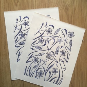 May include: Two white pieces of paper with a blue floral design printed on them. The design features stylized flowers, leaves, and stems.