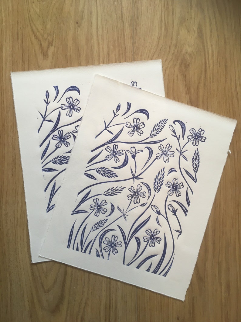 May include: Two white pieces of paper with a blue floral design printed on them. The design features stylized flowers, leaves, and stems.