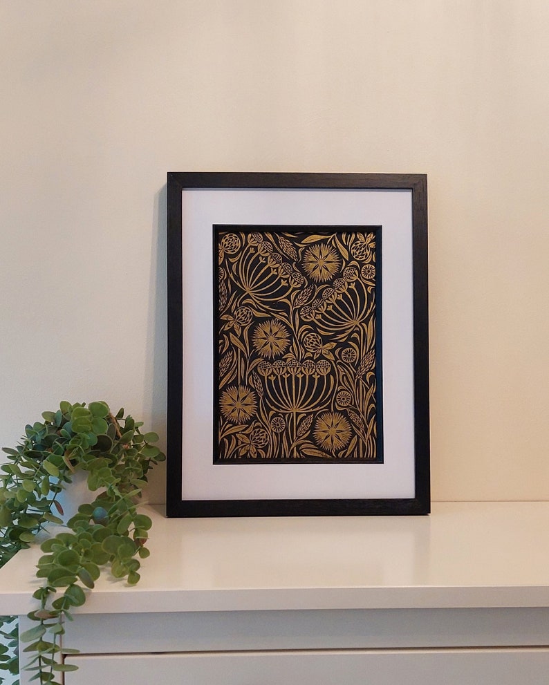 May include: Framed art print featuring a gold floral design on a black background. The artwork is displayed in a black frame with a white mat. The print showcases detailed botanical illustrations, creating a striking contrast.