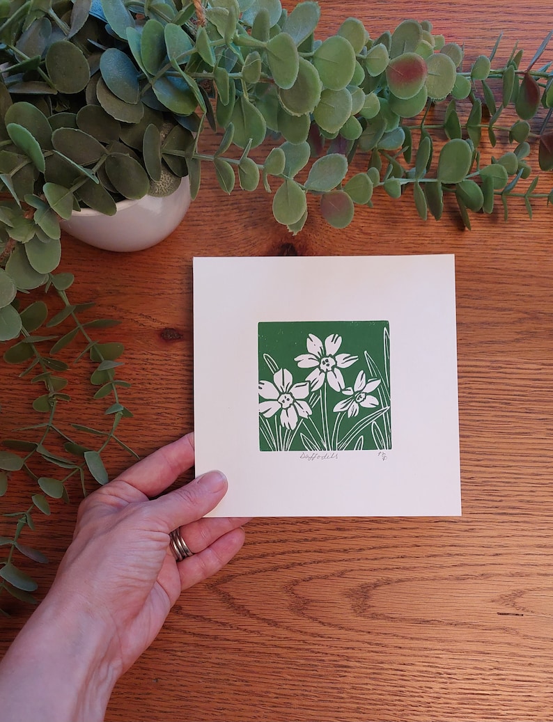 May include: A white card with a green border and a white print of daffodils on a green background. The card says "Daffodils" at the bottom.