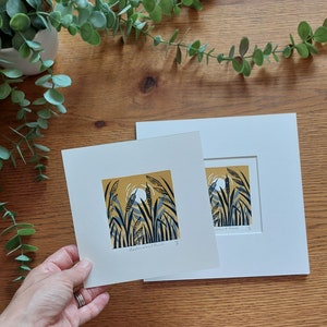May include: A framed print of a nature scene with tall grasses and a yellow moon in the background. The print is titled "Cattails & Reeds".