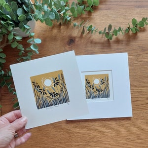 May include: Two framed prints of a yellow field with blue and black flowers and a white sun. The smaller print is titled "Sunny Field".