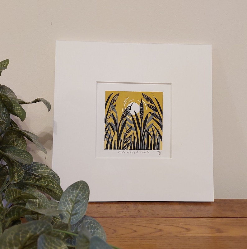 May include: A framed print of a yellow and black illustration of reeds and a bird in a yellow field. The print is titled "Eustmahes & Reeds" and is signed with the number 15.