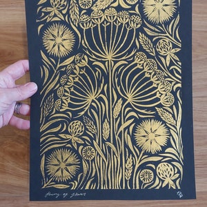 May include: Black and gold floral art print featuring a detailed botanical design. The print showcases stylized flowers and foliage in gold against a black background. The text "flurry of flowers" is written in cursive at the bottom.