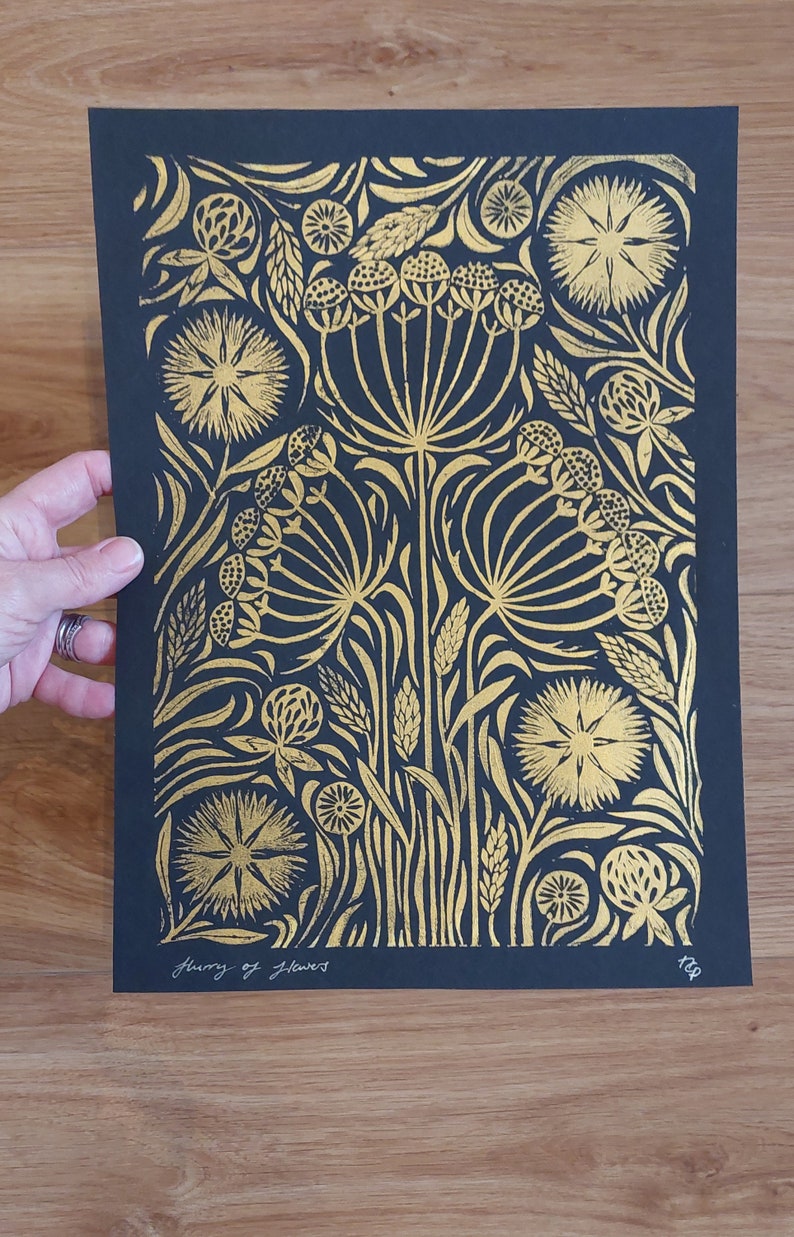 May include: Black and gold floral art print featuring a detailed botanical design. The print showcases stylized flowers and foliage in gold against a black background. The text "flurry of flowers" is written in cursive at the bottom.