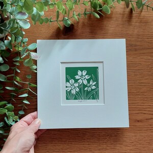 May include: A white mounted print of a green linocut depicting three white daffodils on a green background. The print is signed "Daffodils" and numbered "1/5".
