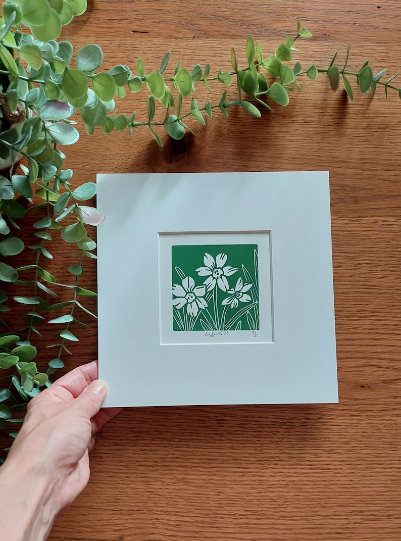 May include: A white mounted print of a green linocut depicting three white daffodils on a green background. The print is signed "Daffodils" and numbered "1/5".