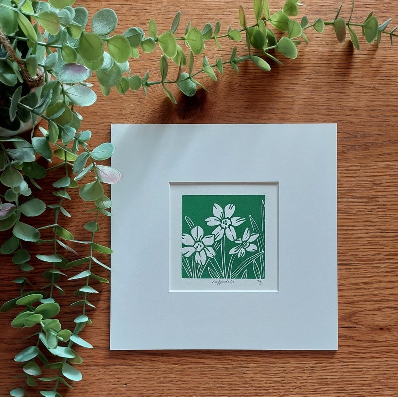 May include: A white matted print of a green linocut featuring three white daffodils on a green background. The print is signed and numbered.