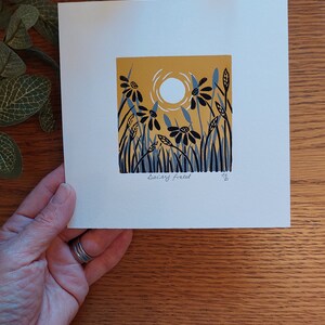 May include: A white card with a yellow background and black and blue stylized flowers. The sun is represented by a white circle. The card is signed "Saicy Freel" in the bottom left corner.