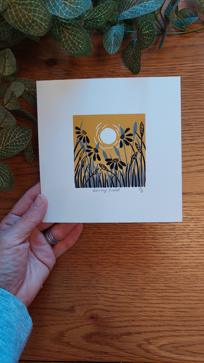 May include: A white card with a yellow background and black and blue stylized flowers. The sun is represented by a white circle. The card is signed "Saicy Freel" in the bottom left corner.