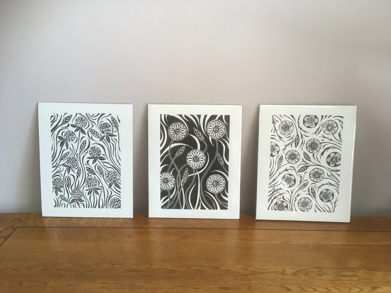 May include: Three black and white floral prints on white paper. The prints feature different floral designs, including clover, dandelions, and other flowers.