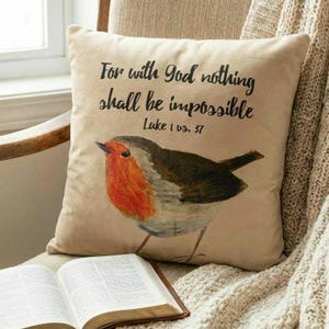 May include: A square cushion in beige with a robin illustration and the text "For with God nothing shall be impossible Luke 1 vs. 37". An open book is visible below the cushion.