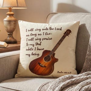 May include: Cushion with a cream background, featuring a brown acoustic guitar illustration and text. The text reads "I will sing unto the Lord as long as I live: I will sing praise to my God while I have my being." Psalm 104 v0.33 is also printed.