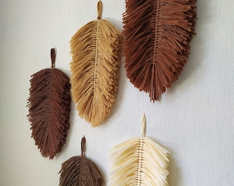 May include: Five brown, beige, and cream colored woven feather wall hangings. The feathers are made of thin strips of material and are arranged in a layered pattern.