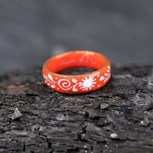 May include: A bright orange ring with a white floral design. The ring is made of metal and has a smooth, polished finish.