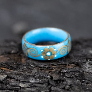 May include: A blue ring with a gold floral design. The ring is made of wood and has a smooth finish.