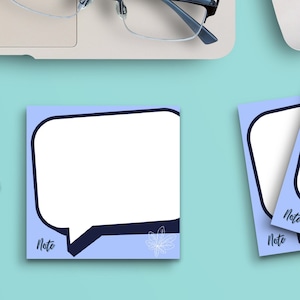 May include: A flat lay of a workspace with a laptop, a white mouse, a cup of coffee, a pair of glasses, and three blue and white speech bubble notepads with the word "Note" printed on them.  There are also four black metal paper clips in the shape of a cat.