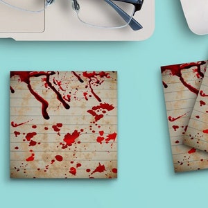 Op de afbeelding: Vier vierkante plakbriefjes met een bloedspat-ontwerp. De briefjes zijn gestreept en hebben een witte achtergrond met rode bloedspatten.