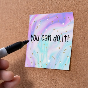 May include: A pink, blue, and purple marble-patterned sticky note with gold glitter and the text "You can do it!" written in black marker.