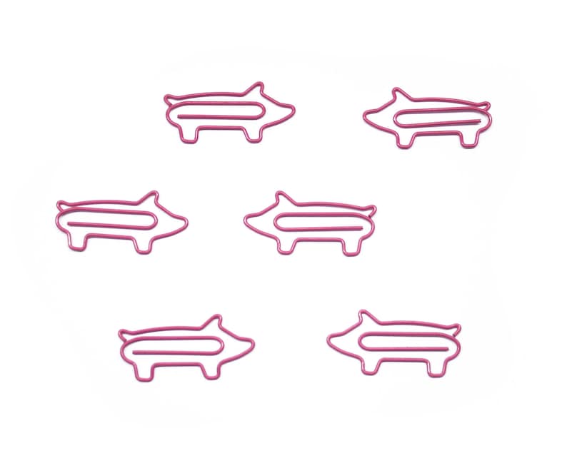 May include: Five pink pig-shaped paper clips. The clips are made of metal and have a shiny finish.